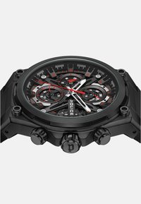 Orologio cronografo analogico nero con quadrante texturizzato, dettagli rossi e tre sotto-quadranti. Presenta una cassa nera robusta e tre pulsanti.