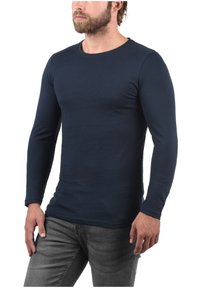 Marineblauwe langemouwen t-shirt van zachte, elastische stof, ronde halslijn, aansluitend ontwerp, gecombineerd met donkergrijze jeans. Geen patronen of hardwaredetails.
