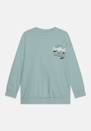 Pull léger en teal, fabriqué en tissu doux. Il présente un col rond et des manches longues. Texte graphique affiché avec un thème cosmique sur le devant.