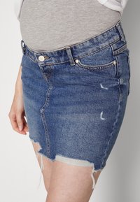 Denimhame, jossa on rispaantunut helma, keskisinisessä värissä. Siinä on klassinen viisi taskun muotoilu ja hienovaraisia kuluneita yksityiskohtia.