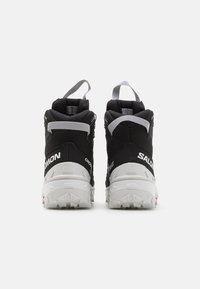 Czarno-białe wysokie buty trekkingowe z teksturowaną syntetyczną cholewką, wyraźnymi wzmocnieniami pięty, pętlami do wkładania oraz solidnymi białymi podeszwami.
