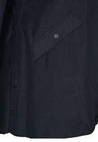 Svart vattentät jacka med en slät yta, som har en diagonalt placerad ficka med knappstängning och knappdetaljer längs fram.