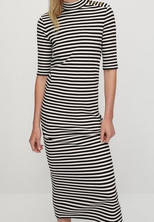 Woman wearing a fitted black and white horizontal striped midi dress with elbow-length sleeves and button details on the shoulder.