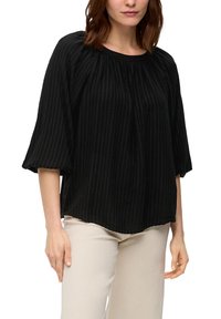 Zwarte blouse met geribbelde textuur, ronde halslijn en driekwart pofmouwen. Lichtgewicht stof valt zachtjes, wat mooi samengaat met beige broeken.