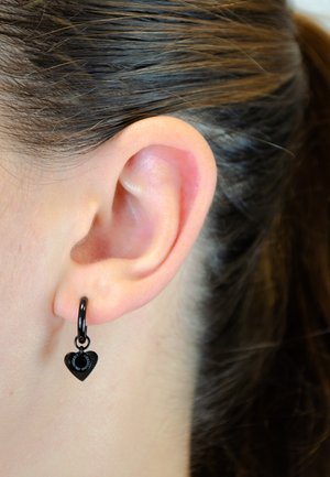Zwart hartvormig oorbelletje met een kleine lusbevestiging, hangend aan de oorschelp, met een gladde, glanzende oppervlakte en subtiele gegraveerde details.