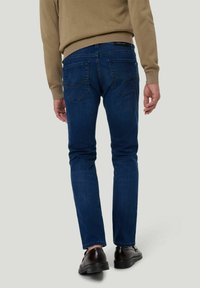 Jean en denim bleu foncé avec une coupe droite, comportant deux poches arrière et des détails de couture subtils, associé à un pull beige.