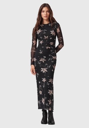Abito nero a maniche lunghe con stampa floreale, design aderente, texture liscia e maniche trasparenti; abbinato a stivali neri alla caviglia.