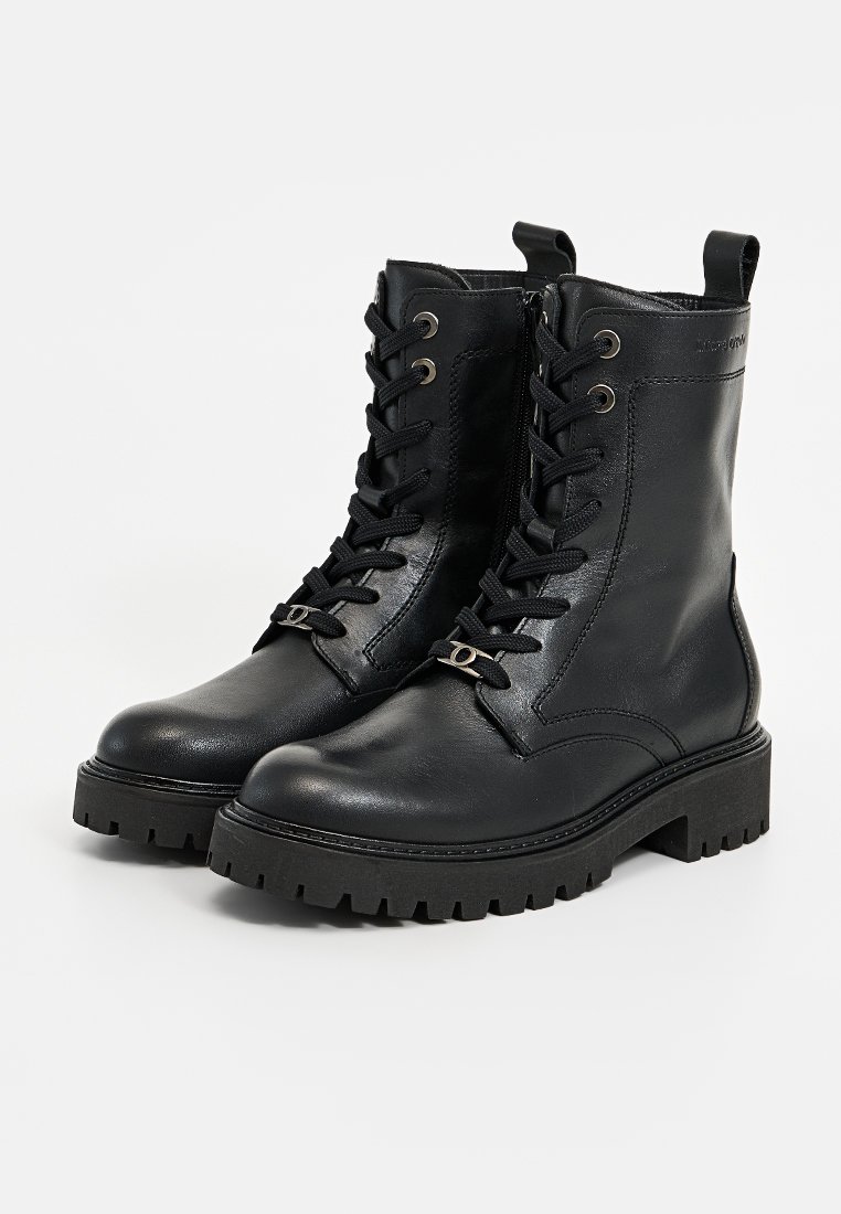 Schwarze Lederknöchelboots mit Schnürung, metallischen Ösen und strukturierten Gummisohlen. Mit einem kleinen dekorativen Metallelement.