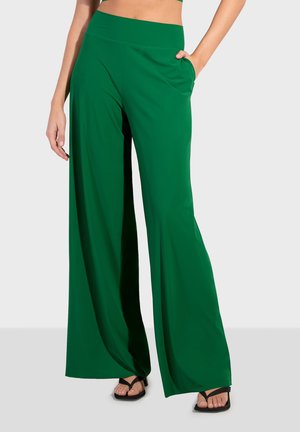 Pantalones de perneras anchas en verde, hechos de una tela suave, con una cintura alta y bolsillos laterales, combinados con chanclas negras.