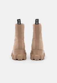 Bottes beige chevilles avec un dessus en tricot gaufré, semelle épaisse et languettes. La semelle présente un motif de crantage distinct pour une meilleure adhérence.