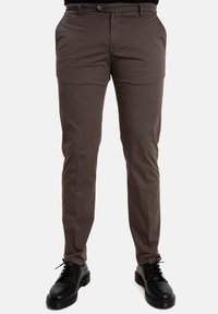 Pantaloni di cotone marroni con una vestibilità slim, dotati di tasche laterali e passanti per cintura, abbinati a scarpe nere stringate con suola spessa.