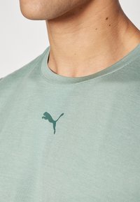 Roheline ümar kaelusega T-särk, mis on valmistatud pehmest kangast ja mille rinnapiiril on tumedamas toonis diskreetne Puma logo.