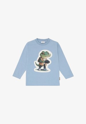 Light blue long-sleeve shirt with cartoon crocodile wearing a vest, sneakers, and backpack, holding a camera.