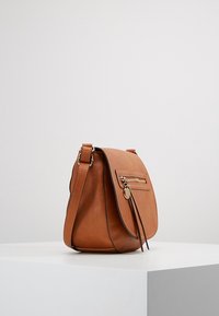 Brązowa skórzana torba na ramię z klapką, przednią kieszenią na zamek i odpinanym paskiem. Charakteryzuje się gładką fakturą i złotymi elementami metalowymi.