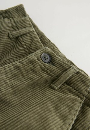 Olivgrüner Cordstoff mit gerippter Textur, der einen runden schwarzen Knopf und eine Gürtelschlaufe zeigt.