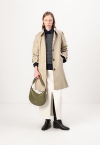 Krémový trench coat s předním zapínáním na knoflíky a ohrnutými rukávy, zkombinovaný s námořnicky pruhovaným svetrem a bílou sukní. Zelená kabelka přes rameno a černé kotníkové boty.