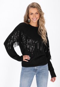 Maglione nero con dettagli a frange lungo lo scollo, decorato con paillettes. Tessuto lavorato a maglia, maniche lunghe, abbinato a jeans azzurri chiari.