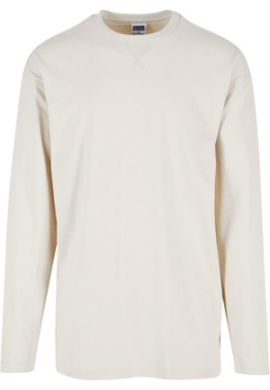 T-shirt à manches longues couleur crème en coton doux, avec un col rond et des fentes sur les côtés pour plus de confort. Design minimaliste, texture unie.