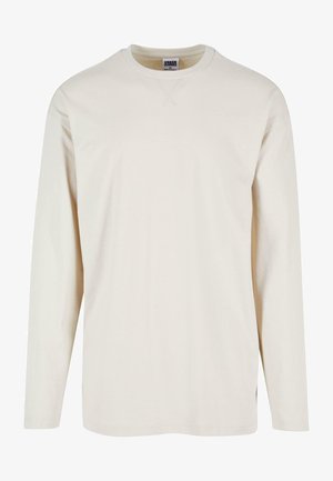 Dlhý rukáv krémové tričko vyrobené z jemnej bavlny, s okrúhlym výstrihom a bočnými rozparky pre väčšie pohodlie. Minimalistický dizajn, obyčajná textúra.
