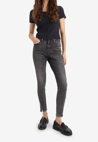 Top corto a maniche corte a coste nere con bottoni, abbinato a jeans skinny grigi a vita alta con cerniere all'orlo, indossato con mocassini neri.