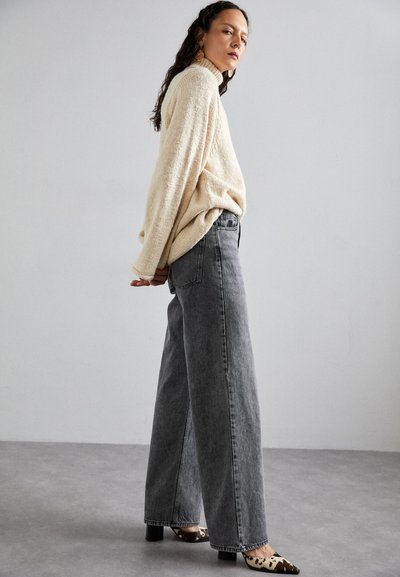 Oversized cream knit sweater, high-waisted gray wide-leg jeans, and leopard print heels, with textured fabric and relaxed fit.