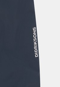 Námořnická modrá tkanina s hladkým povrchem; na straně se nachází vyšívané logo "Didriksons" v bílé barvě, což zdůrazňuje identitu značky.