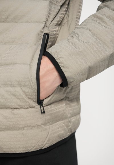 Bež puhasta jakna z odtisom toniranega logotipa "Emporio Armani", stranski žep s črnim zadrgo in črnim elastičnim detajlom na manšetah.