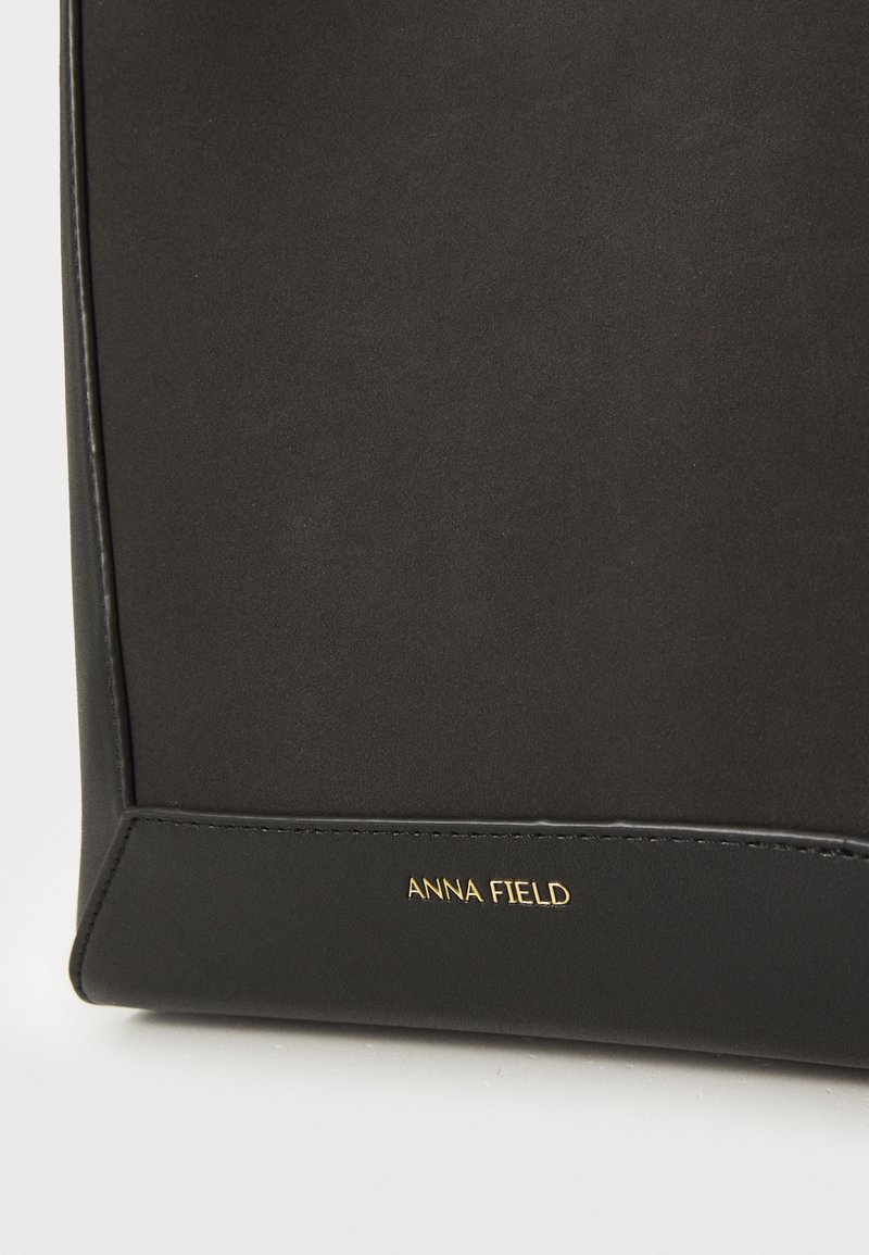 Borsa a tracolla in pelle nera con texture liscia, caratterizzata da un logo in oro impresso e un design minimalista. I bordi sono cuciti per garantirne la durata.