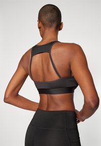 Svart sports-bh med racerback-design, med en bred bånd og et strukturert stoff. Søm detaljer og en slank, tettsittende fasong.