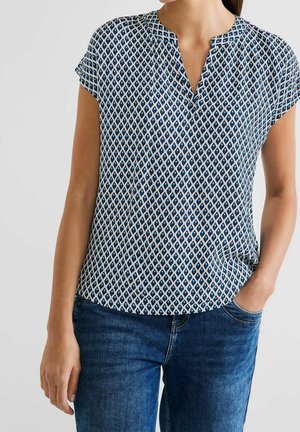 Bluzka z krótkim rękawem w kolorze granatowym, z geometrycznym białym wzorem, dekoltem w kształcie litery V i luźnym krojem. Materiał ma lekką, gładką fakturę.