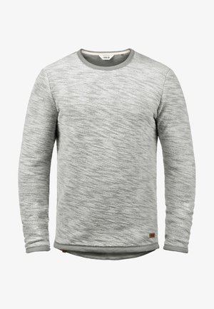 Pull en maille gris clair avec un motif texturé, encolure ronde et manches longues. Présente une petite étiquette en cuir marron en bas de l'ourlet.