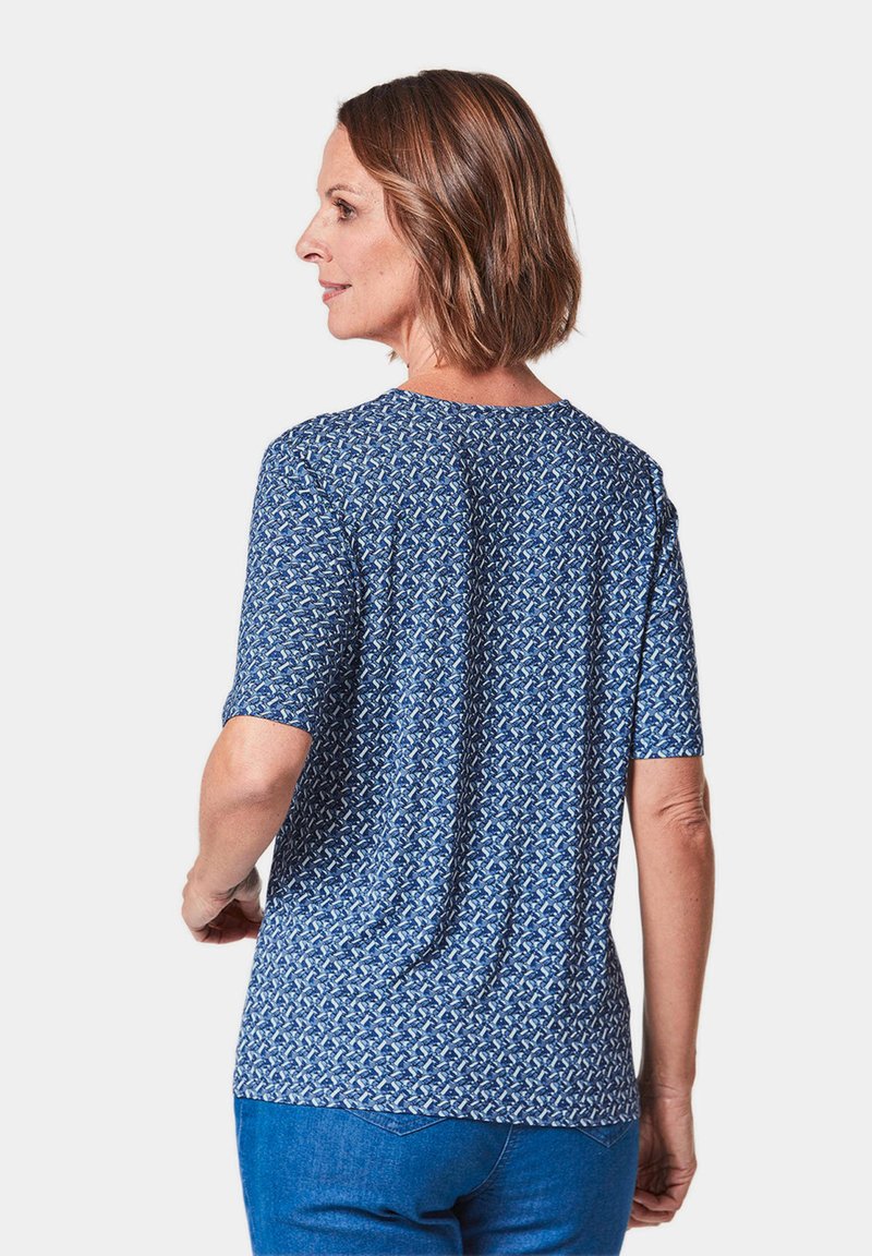 Chemise à manches courtes bleu à motifs avec un col rond, fabriquée en tissu doux. Présente des formes géométriques en blanc et bleu clair.