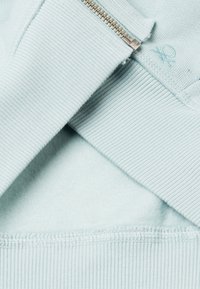 Felpa azzurra chiara con polsini a coste e dettagli con zip; morbida texture interna; cuciture visibili e accento del logo.