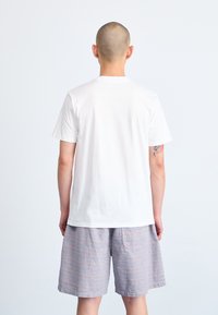 Witte katoenen t-shirt met een losse pasvorm, korte mouwen en een ronde hals, gedragen met een geruite short in licht paarse en grijze tinten.
