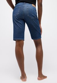 Donkerblauwe denim shorts met een middelhoge taille, vijf zakken en een label op de achterkant. Soepele textuur en rechte snit aan de zoom.