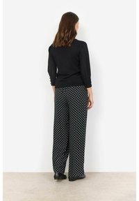 Pullover nero con maniche a tre quarti e dettagli a bottoni, abbinato a pantaloni a gamba larga con pois bianchi e neri.