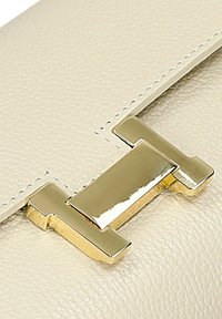 Beige leren handtas met een gestructureerde afwerking en een opvallende gouden sluiting aan de voorkant. Genaaid detail langs de randen.