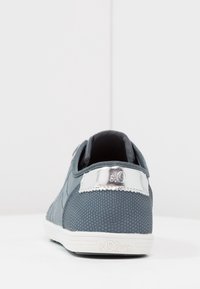 Grå sneaker med strukturerad meshtjocklek, släta silverdetaljer och vit sula. Har en varumärkesetikett vid hälen.