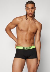 Black boxer briefs with a neon green waistband featuring the "DIESEL" logo, cotton material, fitted design, and smooth texture.