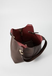 Brown leather tote bag with a textured finish; interior features red lining and a zippered pocket. Includes a decorative hardware accent.