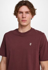 Mørkerød bomulds t-shirt med korte ærmer, rund hals og et lille cremefarvet chevron-logo accent på venstre bryst.