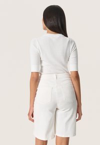 White ribbed short-sleeve top paired with high-waisted white denim shorts. The shorts have a clean design with back pockets and light texture.