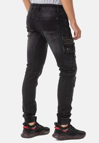 Pantalons cargo en denim noir avec une coupe ajustée, poches latérales zippées et logo brodé au dos. Complétés par des baskets noires.