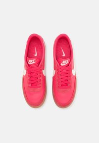 Paire de baskets Nike rose vif avec logos Swoosh blancs et semelles marron, affichées côte à côte sur un fond blanc.