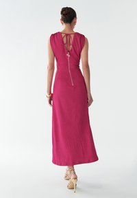 Fuchsia sleeveless maxi dress with a scoop back, tie detail at the neck, and a side zipper; smooth texture and floor-length design.