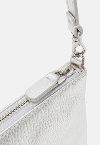 Hopealakka hopeanvärisestä metallista valmistettu laukku, jossa on teksturoitu pinta, vetoketjusuljin ja hopea varusteet. Varustettu irrotettavalla hihnalla monipuolisuuden lisäämiseksi.