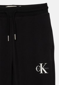 Melni sporta bikses no kokvilnas maisījuma, ar elastīgu jostasvietu, auklu un baltu Calvin Klein logo, kas izdrukāts kreisajā augšstilbā.
