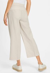 Beige linen cropped pants with an elastic waistband, two back pockets, and a relaxed fit, paired with white platform sneakers.