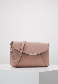 Světle růžová kožená kabelka se stříbrným řetízkovým popruhem a obdélníkovou kovovou sponou, vystavená na bílé podstavě na jednobarevném pozadí.