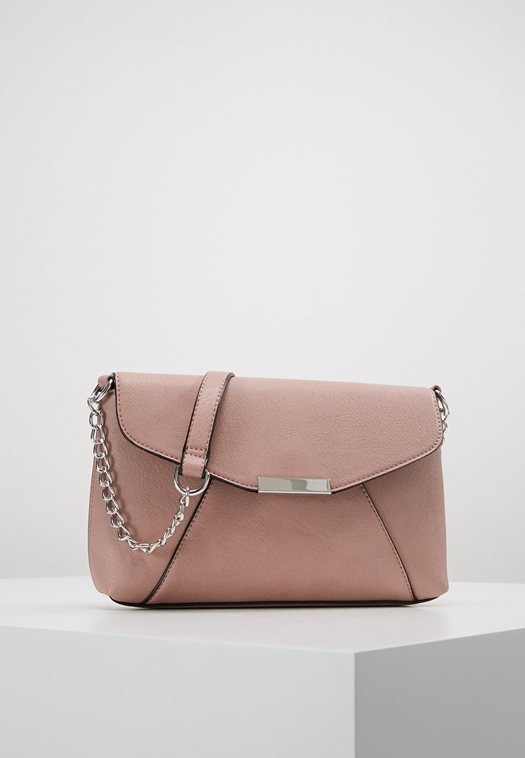 Světle růžová kožená kabelka se stříbrným řetízkovým popruhem a obdélníkovou kovovou sponou, vystavená na bílé podstavě na jednobarevném pozadí.